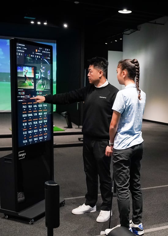 Lead coach Daniel Cho analyzing a golf student's swing data on a launch monitor.