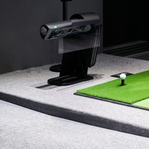 Close-up of a golf ball on a tee next to the floor-mounted RangeX launch monitor sensor on a green turf mat.